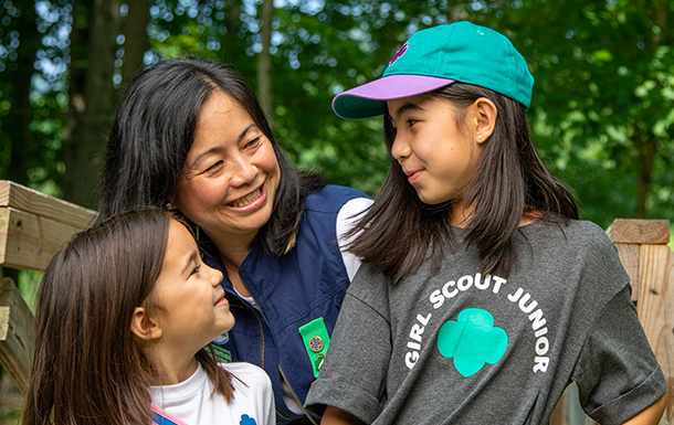 Troop leader with two Girl Scouts smiling outdoors